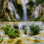 A powerful, wide waterfall cascading down a lush green cliff surrounded by dense tropical rainforests in Athirappilly, Kerala.