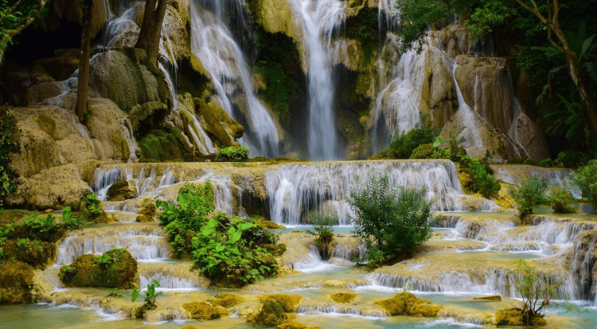A powerful, wide waterfall cascading down a lush green cliff surrounded by dense tropical rainforests in Athirappilly, Kerala.